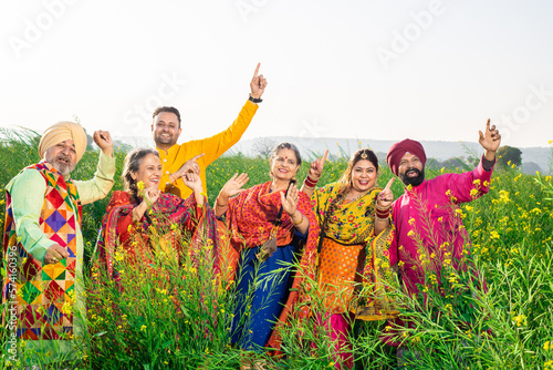 Punjabi sikh family doing bhangra dance in agriculture field celebrating Baisakhi or vaisakhi festival.