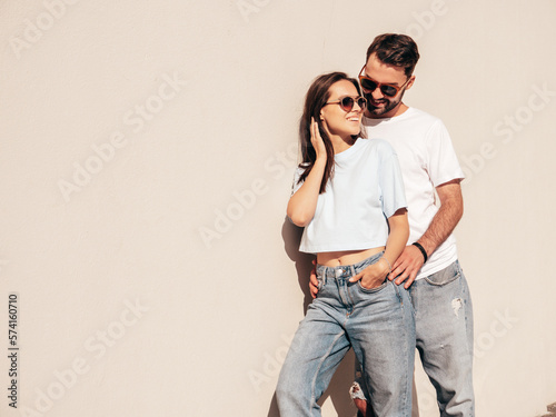 Smiling beautiful woman and her handsome boyfriend. Woman in casual summer jeans clothes. Happy cheerful family. Female having fun. Sexy couple posing in the street near wall. In sunglasses