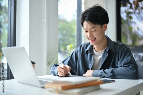 Happy and good-looking young Asian male college student designing his artwork on digital tablet