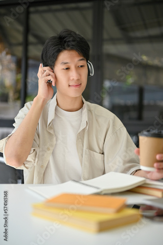 Portrait of happy Asian man listening to music through headphones while relaxing in the cafe.