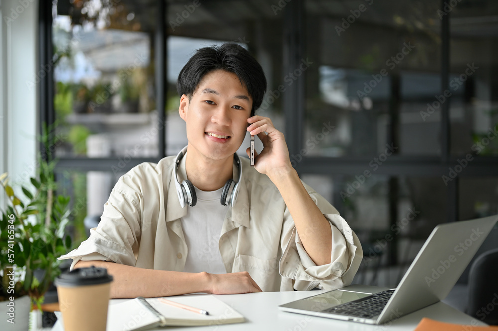 Handsome Asian man on the phone with someone while remote working at the coffee shop Handsome Asian man on the phone with someone while remote working at the coffee shop