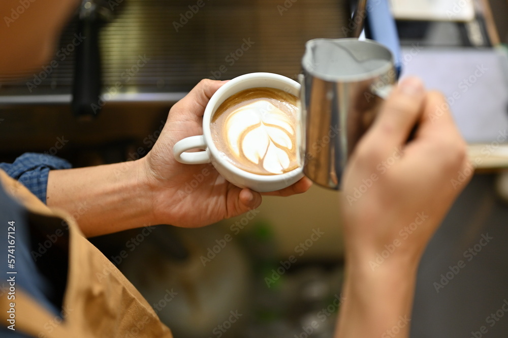 Close-up image, An Asian male barista holding a beautiful latte cup, making beautiful latte art