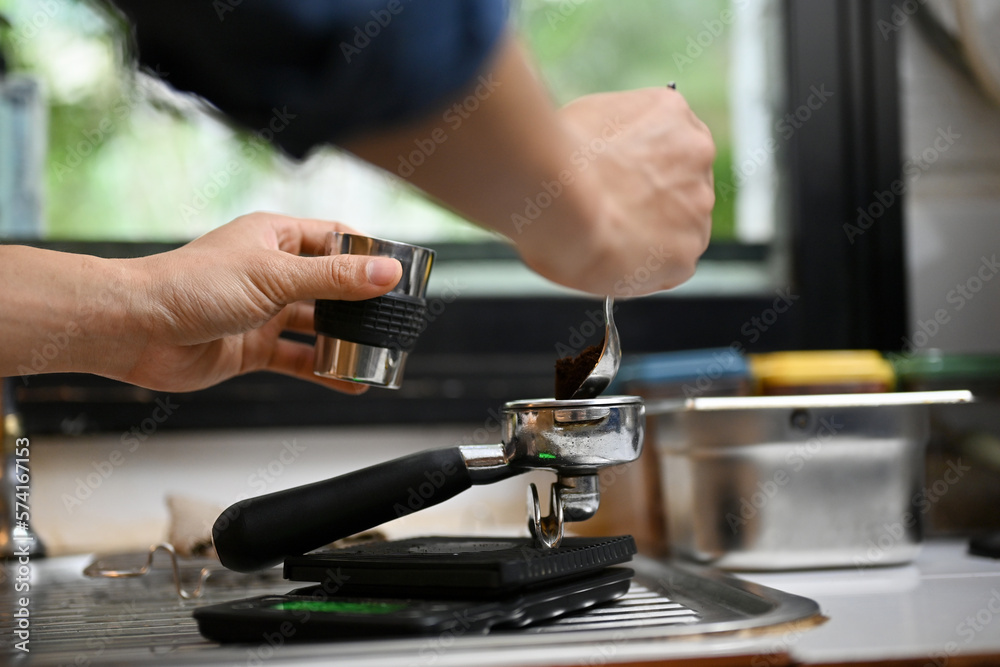 Close-up image of a male barista making an espresso shot, adding coffee powder into a portafilter.