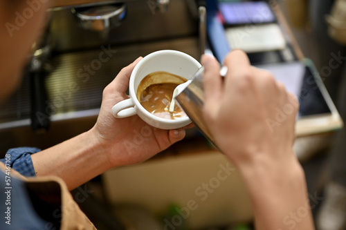 Talented male barista pouring steamed milk into a cup, making beautiful late art