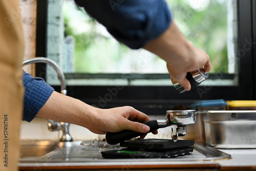 Close-up image of a professional male barista adding coffee powder into a portafiler