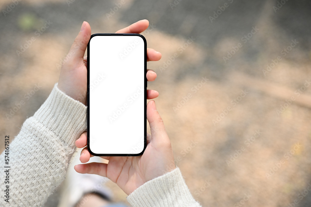 A woman holding a smartphone white screen mockup over blurred street in background. - obrazy, fototapety, plakaty 