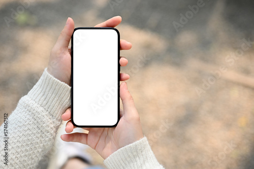 Fototapete A woman holding a smartphone white screen mockup over blurred street in background