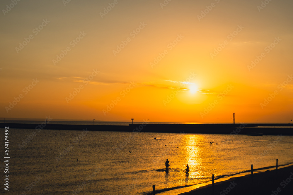 Silhouette of people enjoying sea and summer days. Reflection of sunlight over sea surface at sunset. Orange and gold blue sky. Dramatic Yellow sun coming out of the sea. Majestic summer landscape