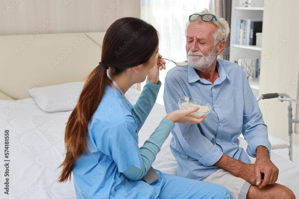 Happy caregiver feeding senior old man on bed with rice porridge soup for breakfast at retirement house. Asian smiling nurse taking good help care and support elder patient at home. Happy caregiver feeding senior old man on bed with rice porridge soup for breakfast at retirement house. Asian smiling nurse taking good help care and support elder patient at home.