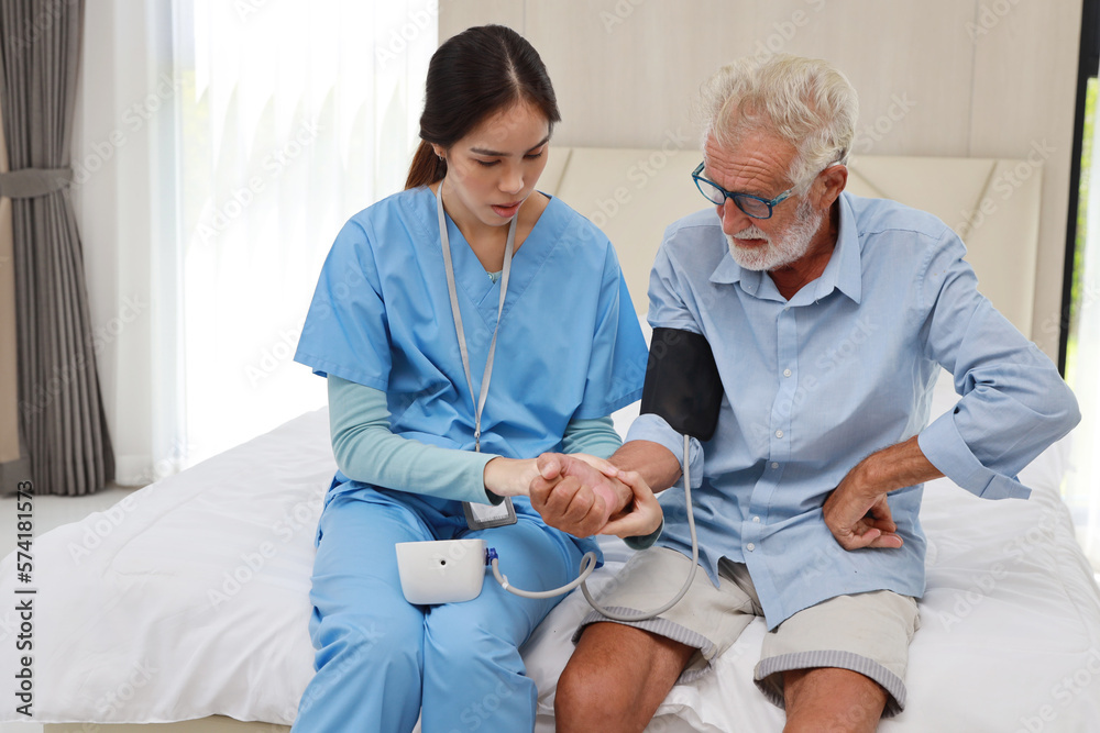 Obraz premium Happy caregiver checking blood pressure monitor and heart rate senior elderly man patient on bed at retirement house. Asian smiling nurse taking good help care and support of elder patient at house