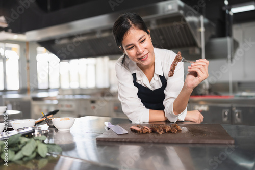Fotografiet Happy student Asia woman chef with steak at kitchen background