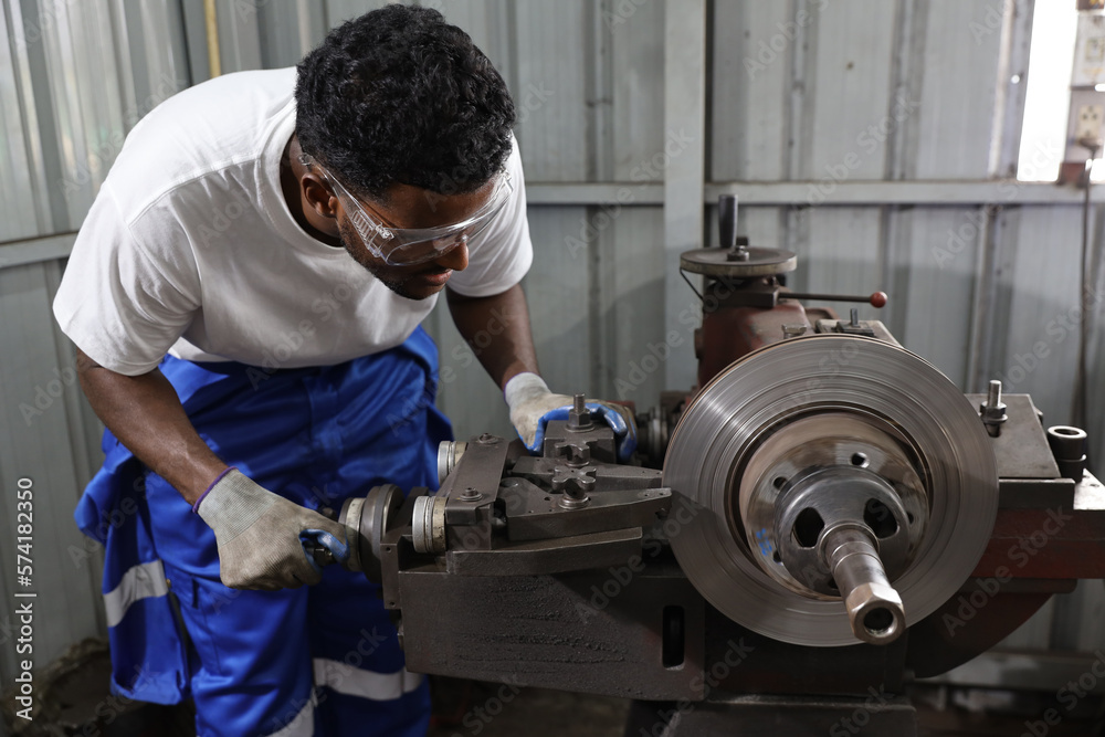 Multiethnic technicain mechanic or worker man in protective uniform using metal lathe machine operate polishing car disc brake at garage. Maintenance automotive and inspecting vehicle part concept Multiethnic technicain mechanic or worker man in protective uniform using metal lathe machine operate polishing car disc brake at garage. Maintenance automotive and inspecting vehicle part concept