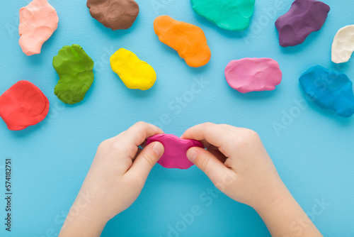 Foto Baby boy hands holding and kneading modeling clay on light blue table background