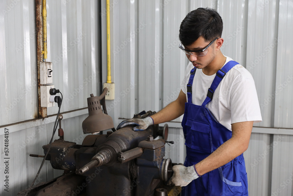 Technician mechanic or worker man in protective uniform using metal lathe machine operate polishing car disc brake at garage. Maintenance automotive and inspecting vehicle part concept Technician mechanic or worker man in protective uniform using metal lathe machine operate polishing car disc brake at garage. Maintenance automotive and inspecting vehicle part concept