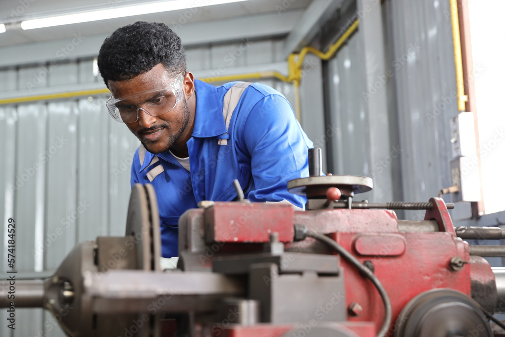 Technician mechanic or worker man in protective uniform using metal lathe machine operate polishing car disc brake at garage. Maintenance automotive and inspecting vehicle part concept