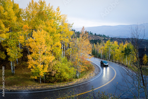 A car drives a curvy mountain road in the rain, aspen trees in golden fall colors