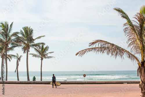 Boy with surfboard on promenade with palm trees at Golden Mile beach, Durban, KwaZulu-Natal, South Africa photo