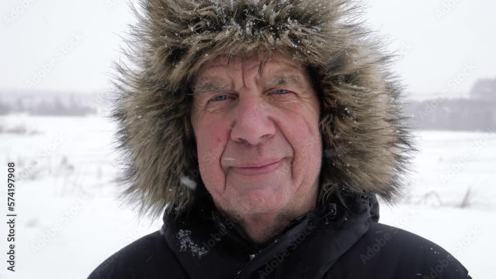 Portrait old elderly man with wrinkles on face. Warm dressed in fur hat standing outside in snowfall frost winter. Walking for health in fresh air. Northern life in arctic circle. Looks at camera calm Portrait old elderly man with wrinkles on face. Warm dressed in fur hat standing outside in snowfall frost winter. Walking for health in fresh air. Northern life in arctic circle. Looks at camera calm