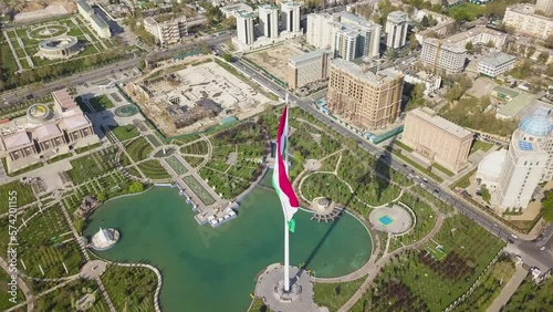 Dushanbe city center landmarks and flag of Tajikistan. Aerial cinematic shot over a Rudaki park and national library.
