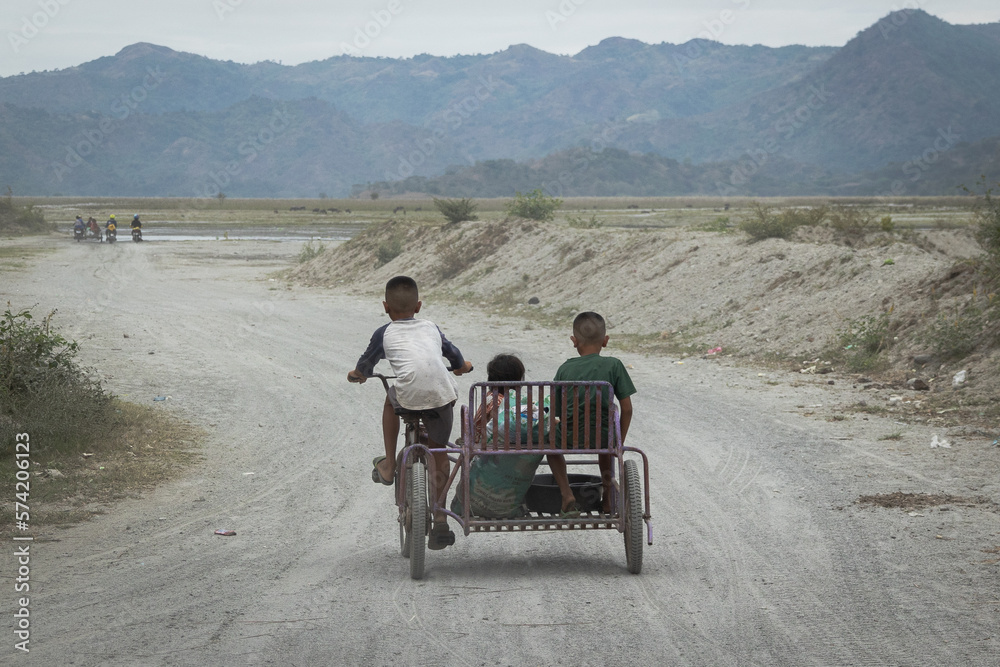 Three kids traveling along a dusty dirt road at the bottom of a volcano in the Philippines