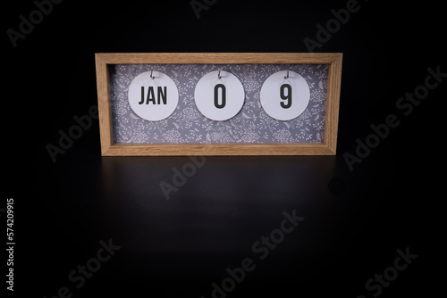 A wooden calendar block showing the date January 9th on a dark black background