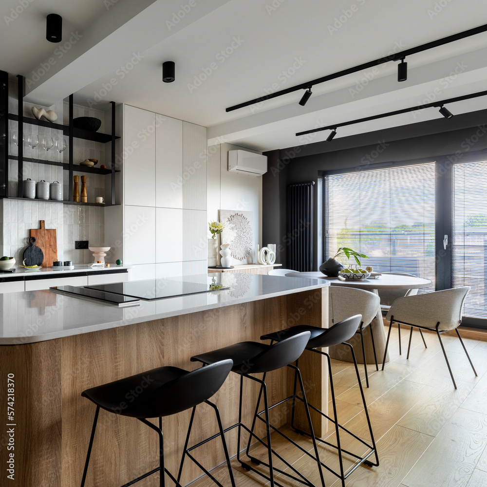 Fototapeta premium Modern composition of kitchen interior with kitchen island, stylish black chockers, built-in kitchen, glass cabinets, grey table and personal accessories. Home decor. Template.