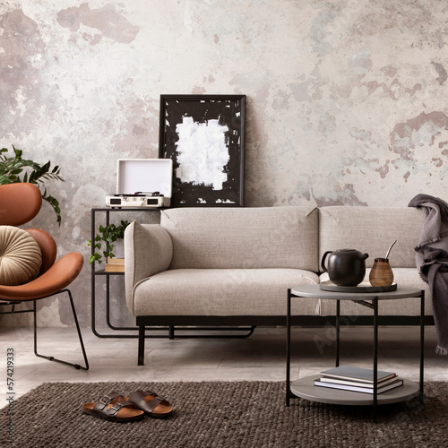 Creative composition of indiustral and loft living room interior with mock up poster frame, gray sofa, round coffee table, brown leather armchairs, plaid, pillows and accessories. Home decor. Template photo