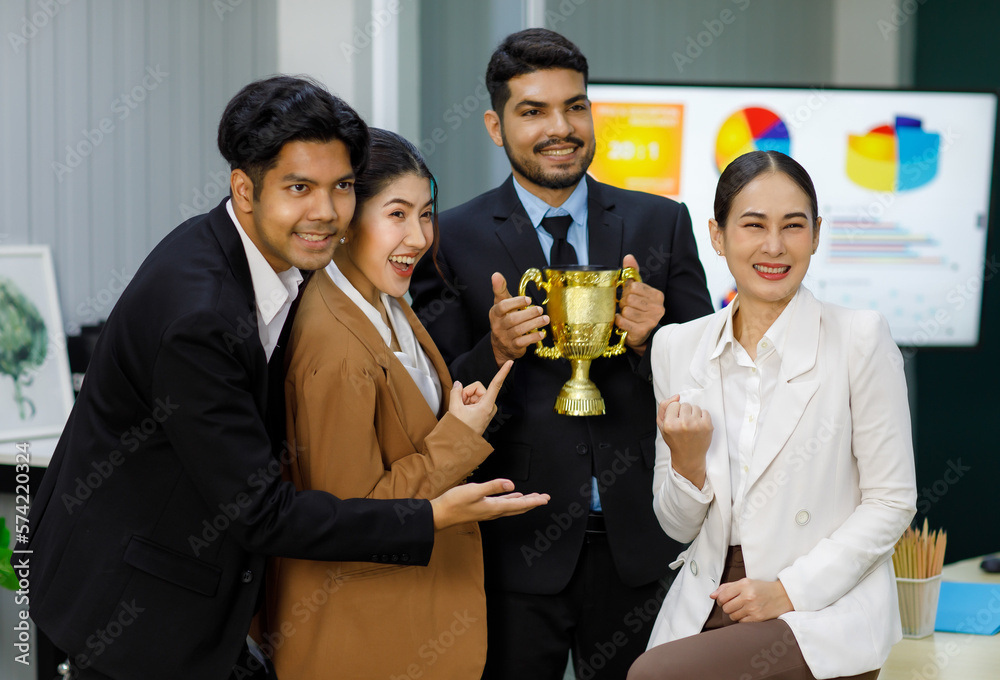 Millennial Asian Indian professional successful bearded businessman in formal suit smiling winning holding business competition golden reward trophy while male female colleagues celebrating together Millennial Asian Indian professional successful bearded businessman in formal suit smiling winning holding business competition golden reward trophy while male female colleagues celebrating together