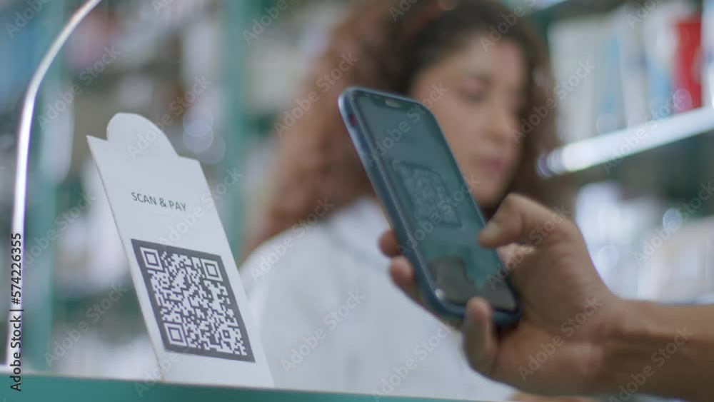 A close-up shot of a hand of a customer scanning a barcode to pay e-money to an electronic bank account or online UPI transfer in a medical store or pharmacy with a smiling woman in the background