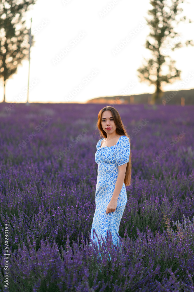 Attractive slender happy girl in a blue dress in a lavender field at sunset. Attractive slender happy girl in a blue dress in a lavender field at sunset.