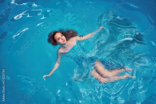 A girl in the water in the pool. The shooting angle from above. The dress is blue.
