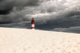 Ein Leuchtturm an einem weißem Sandstrand mit schwarzen Wolken von einem Sturm