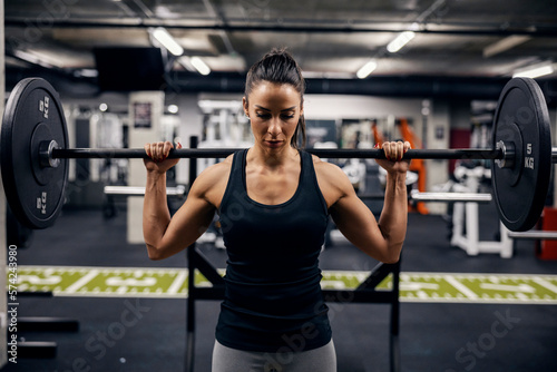 Portrait of a muscular strong female bodybuilder lifting weights in a gym.
