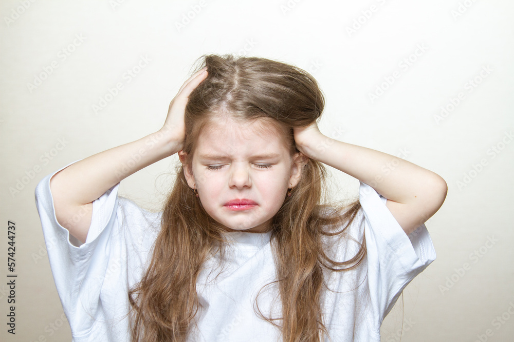Portrait of a cute little blonde girl showing emotions, screaming and pulling her hair. A young girl screams in pain and holds her head.