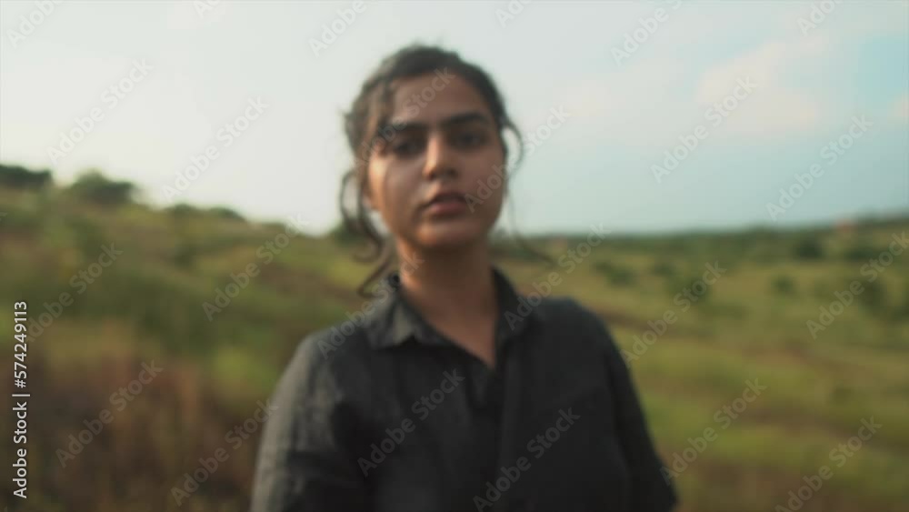 Young adolescent woman in a black dress looking confident into the camera. bright weather, the sun shines on her.