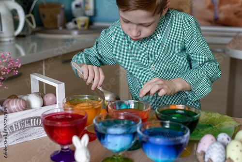 A beautiful sweet and funny red -haired boy paints eggs in the kitchen for Easter. Colored eggs  the child paints at home. Close -up