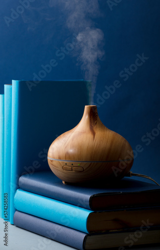 Wooden vaporizer with vapor of natural oils, with different ranges of blue, on the gray table in the living room