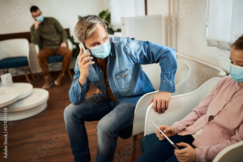 Canvas Print Single father talks on cell phone while being with his daughter in waiting room at clinic