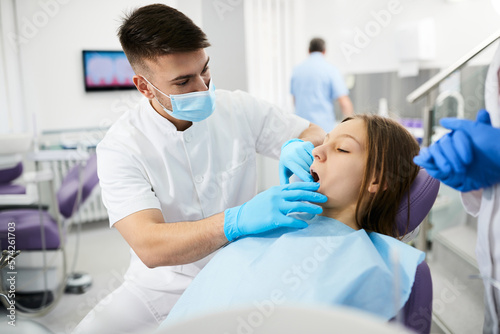 Young dentist doing teeth examination of teenage girl at dental clinic.