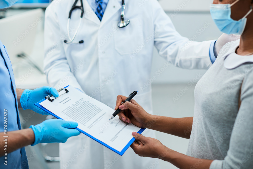 Close up of African American woman signing an agreement at dental clinic .
