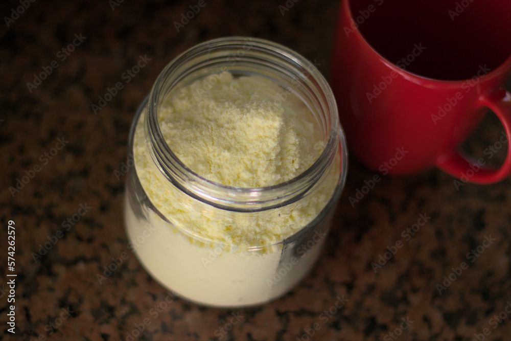 Glass container full of powdered milk along with a red cup. Natural light. Glass container full of powdered milk along with a red cup. Natural light.