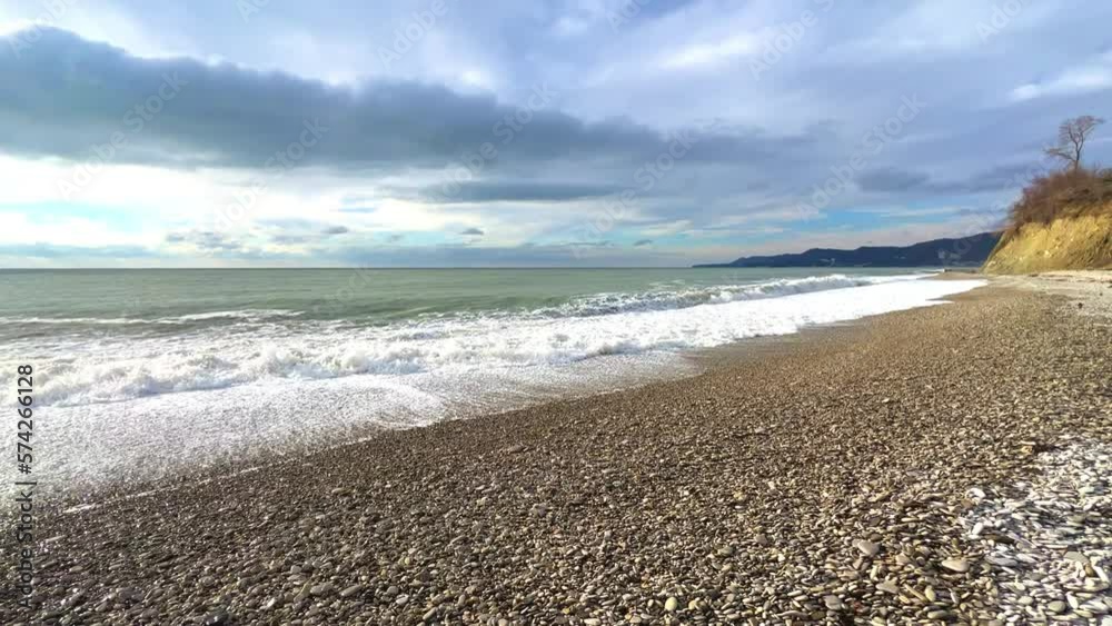 Powerful sea waves are crashing on the Black Sea coast. Waves splash on the beach with pebbles during a storm. Storm at sea. Panoramic view of the Black Sea. Russia. Sunset on the beach. 4K