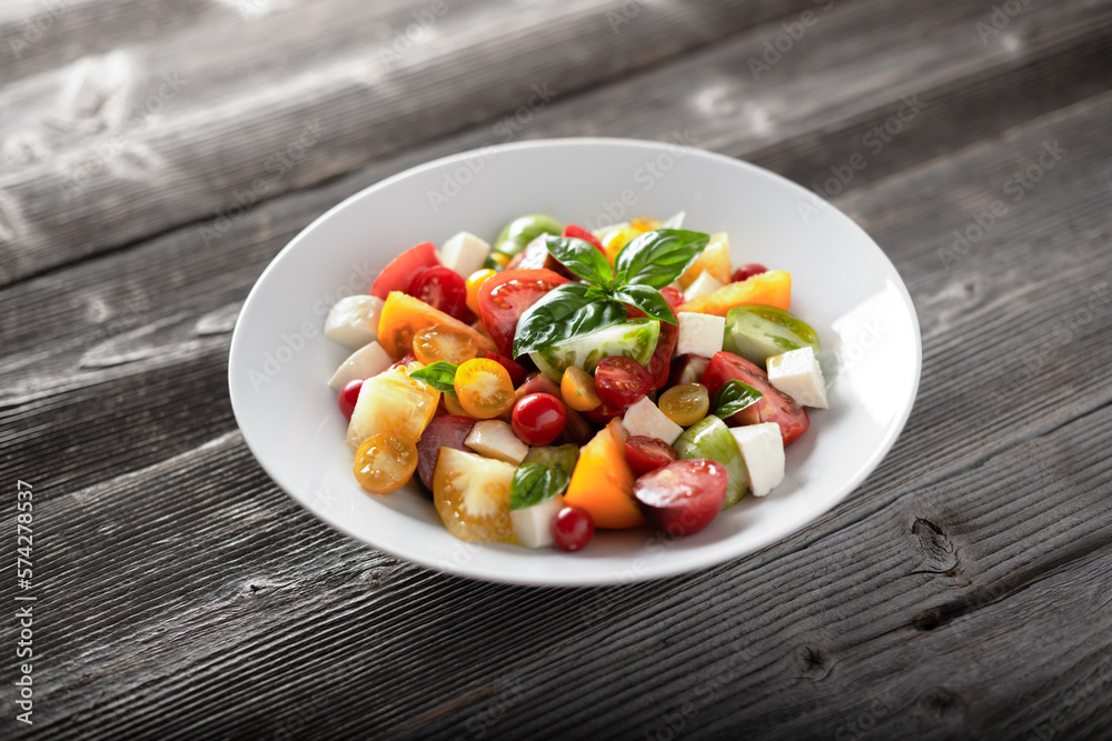 Salad with different varieties kind of red, yellow, green and black tomato mix, mozzarella cheese and basil. Caprese salas with fresh colourful tomatoes. Food photography