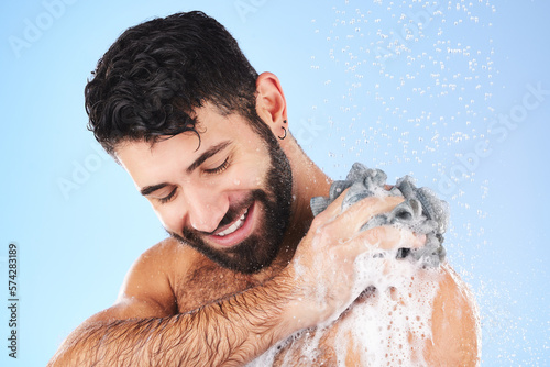 Shower, loofah and man in studio for grooming, hygiene and wellness with soap against blue background. Body care, skincare and male model relax with luxury, foam and product, exfoliation and cleaning photo