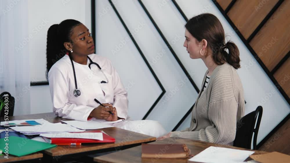 Friendly and Cheerful African American Black Woman Doctor Writing Medical History, Medicine Prescription of Young Female Patient During Consultation in a Health Clinic. Hospital. Health Check Up Exam Friendly and Cheerful African American Black Woman Doctor Writing Medical History, Medicine Prescription of Young Female Patient During Consultation in a Health Clinic. Hospital. Health Check Up Exam