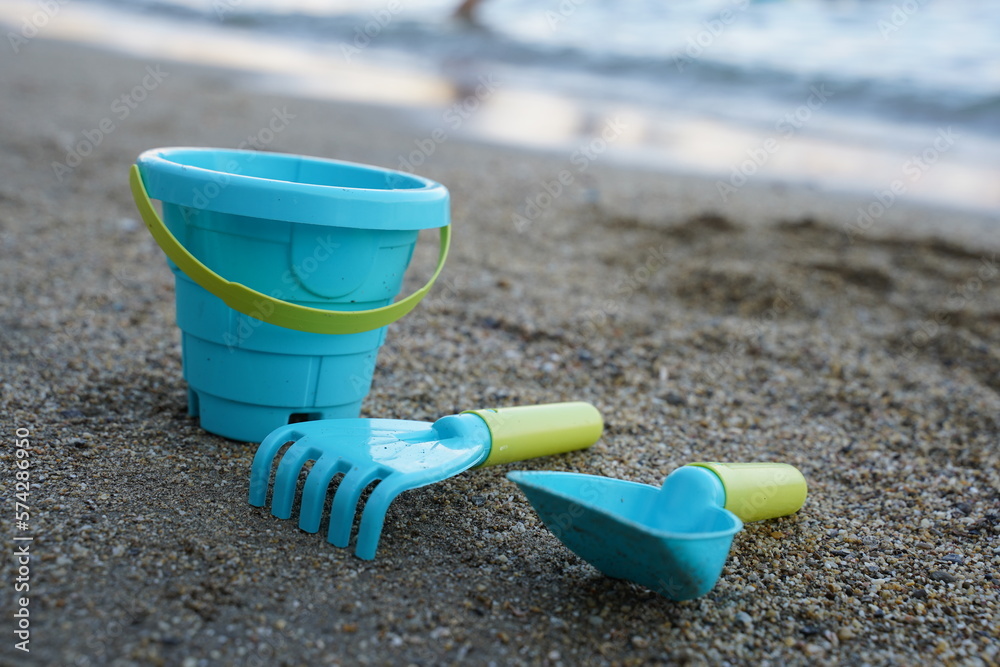 Children's beach toys, bucket, shovel and rake on the sand on a sunny day. The concept of summer holidays with children. Children's beach toys, bucket, shovel and rake on the sand on a sunny day. The concept of summer holidays with children.