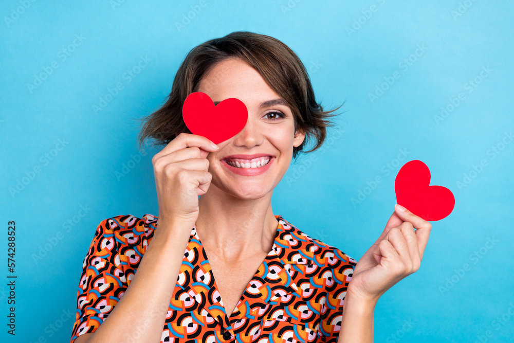 Photo of pretty charming lady dressed print shirt eye cover little red heart isolated blue color background Photo of pretty charming lady dressed print shirt eye cover little red heart isolated blue color background