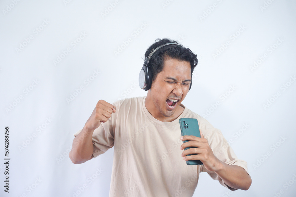 Energized man sings to music, moves actively, wears headphones and casual t shirt, poses against white background, keeps mouth widely opened, enjoys life, isolated on white studio wall Energized man sings to music, moves actively, wears headphones and casual t shirt, poses against white background, keeps mouth widely opened, enjoys life, isolated on white studio wall