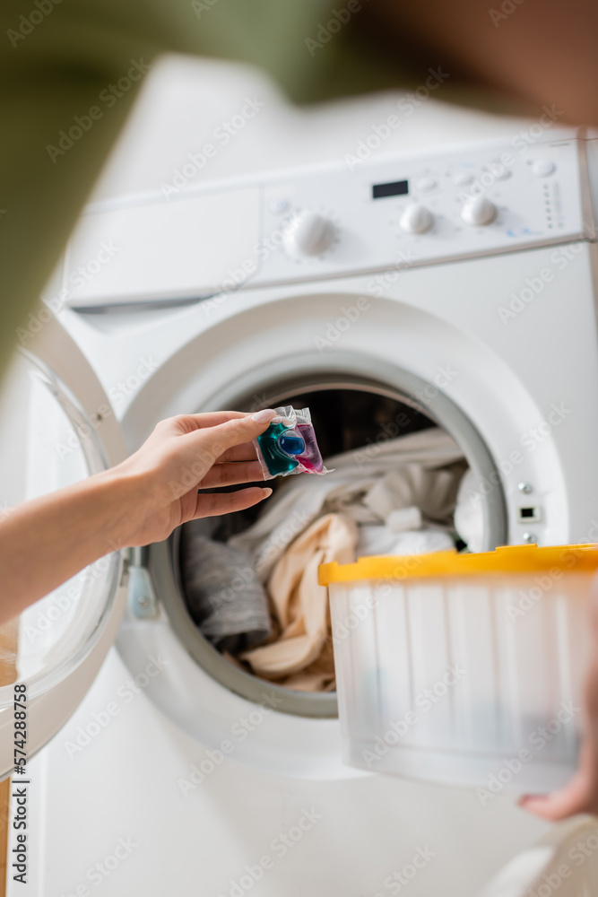 Cropped view of woman holding detergent pod near washing machine with laundry. Cropped view of woman holding detergent pod near washing machine with laundry.