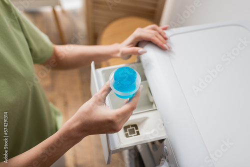 Cropped view of woman holding cap with liquid cleaner near washing machine.